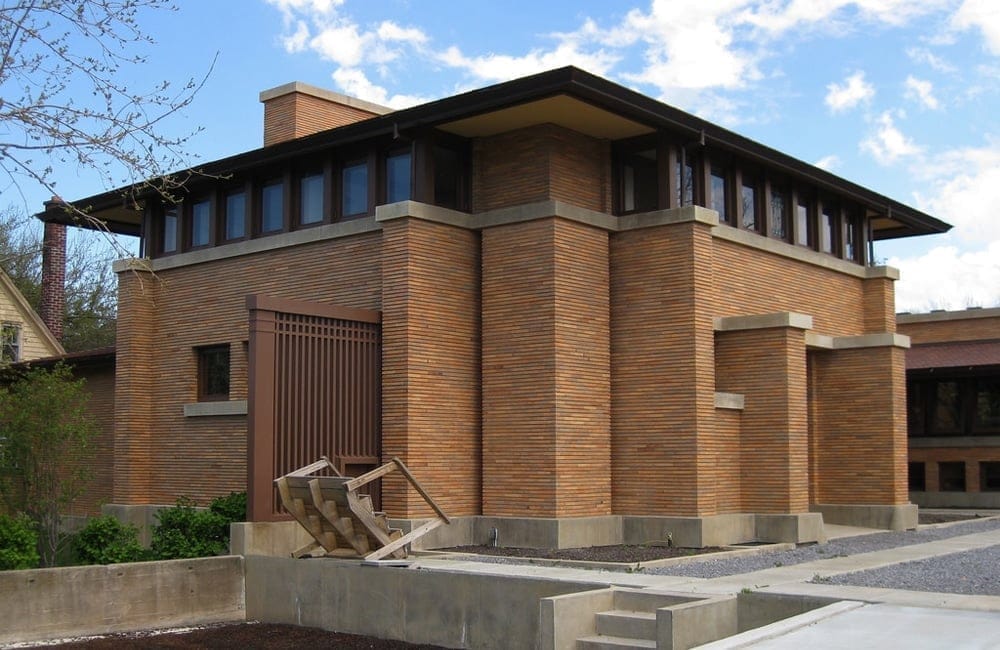 A two-story brick building with a modern design features large windows and a flat roof, reminiscent of the Theodore Roosevelt Inaugural Site. Concrete accents and a metal staircase enhance its geometric aesthetic, all under a partly cloudy sky. A two-story brick building with a modern design features large windows and a flat roof, reminiscent of the Theodore Roosevelt Inaugural Site. Concrete accents and a metal staircase enhance its geometric aesthetic, all under a partly cloudy sky.