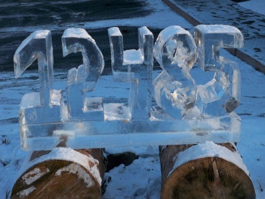 An ice sculpture of the numbers 12485 is displayed outdoors on two wooden logs in Tannersville, surrounded by snow. The clear ice partially reflects light, creating a shimmering effect against the snow-covered ground. An ice sculpture of the numbers 12485 is displayed outdoors on two wooden logs in Tannersville, surrounded by snow. The clear ice partially reflects light, creating a shimmering effect against the snow-covered ground.