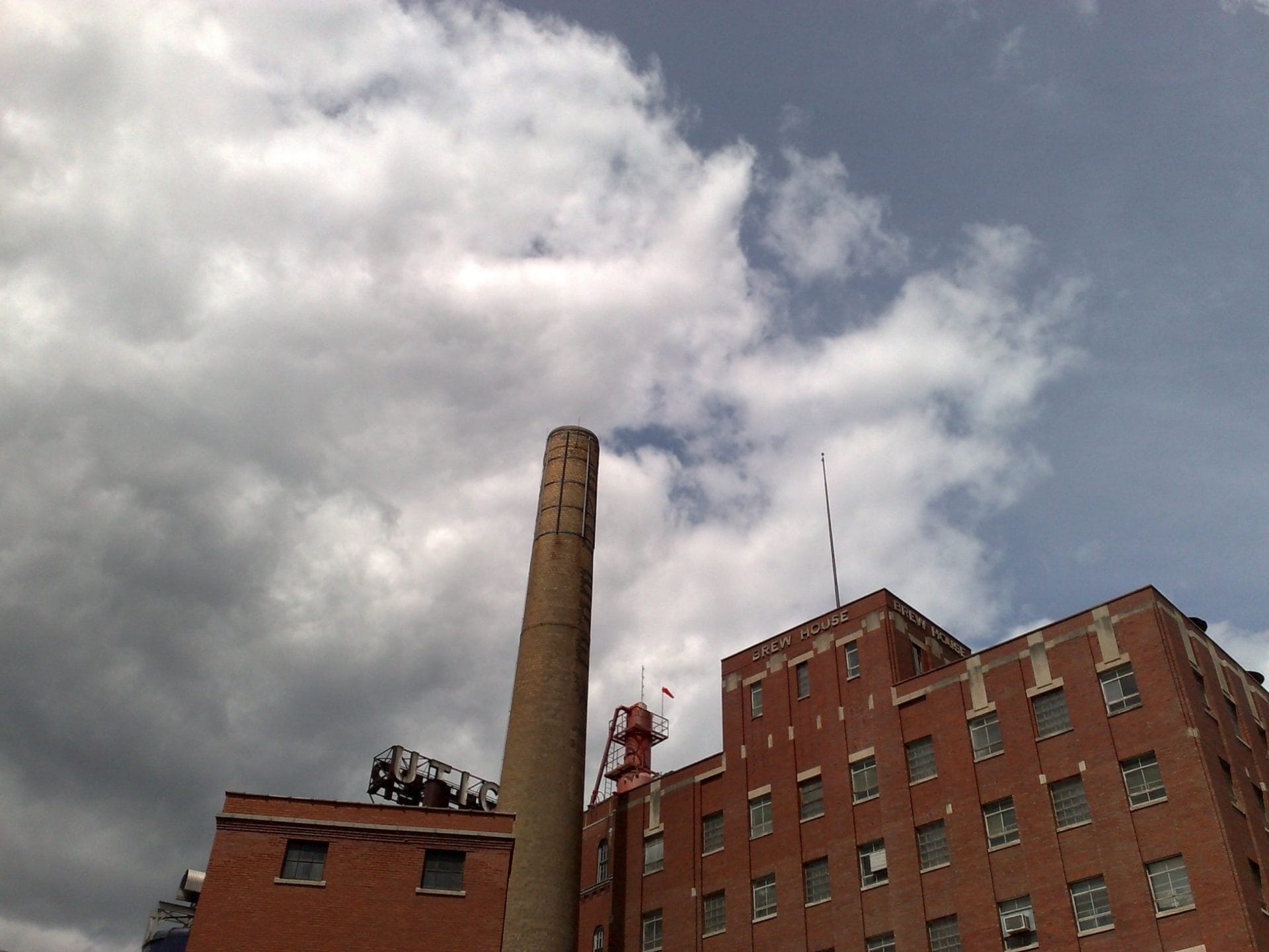 A tall brick chimney and an industrial-style building with a sign partially reading COCA COLA under a cloudy sky. This historic structure, reminiscent of the areas craft beverage heritage, boasts multiple stories of intricate brickwork, with an attached antenna and rooftop equipment. A tall brick chimney and an industrial-style building with a sign partially reading COCA COLA under a cloudy sky. This historic structure, reminiscent of the areas craft beverage heritage, boasts multiple stories of intricate brickwork, with an attached antenna and rooftop equipment.