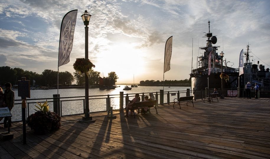 A scenic view of a wooden pier at sunset, with flags waving in the brisk fall breeze. Benches line the waterfront where people embrace the autumn fun. A ship is docked on the right, and wispy clouds fill the sky, creating a serene atmosphere reminiscent of an Amtrak journey through natures beauty. A scenic view of a wooden pier at sunset, with flags waving in the brisk fall breeze. Benches line the waterfront where people embrace the autumn fun. A ship is docked on the right, and wispy clouds fill the sky, creating a serene atmosphere reminiscent of an Amtrak journey through natures beauty.