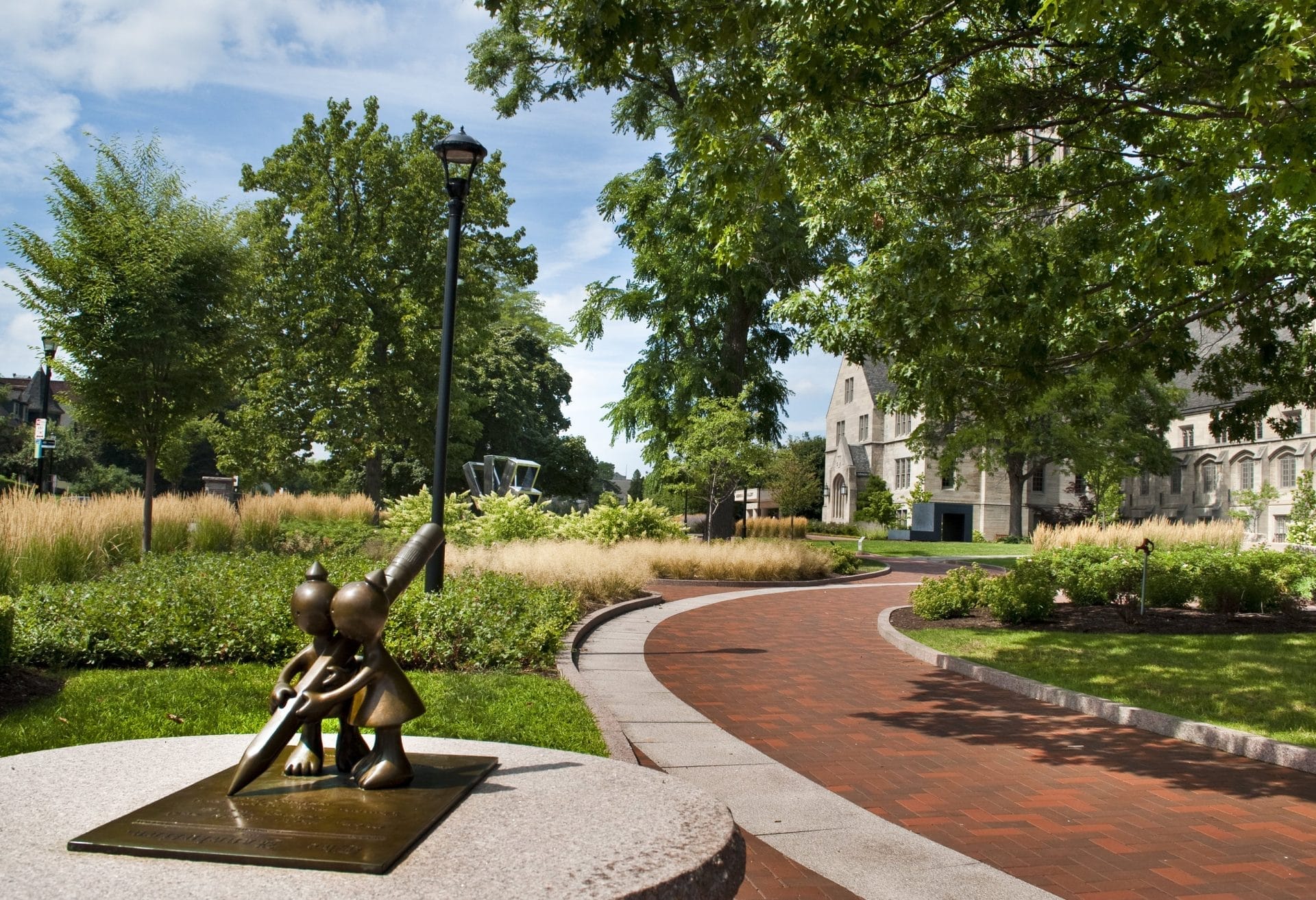 Nestled in a serene setting, this New York sculpture park is worth visiting for its bronze statue of two children peering through a telescope atop a stone pedestal. A brick path meanders through lush greenery, leading to a historic stone building beneath the partly cloudy sky. Nestled in a serene setting, this New York sculpture park is worth visiting for its bronze statue of two children peering through a telescope atop a stone pedestal. A brick path meanders through lush greenery, leading to a historic stone building beneath the partly cloudy sky.
