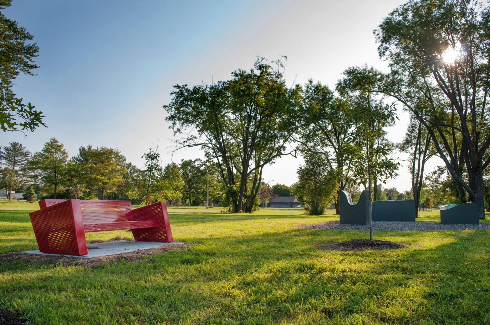 A red, modern-style bench is situated on a grassy field in a park. Nearby, a tree casts shade as the sun peeks through the branches. In the backdrop of this New York sculpture park worth visiting, various trees and an eye-catching sculpture enhance the scenic outdoor setting. A red, modern-style bench is situated on a grassy field in a park. Nearby, a tree casts shade as the sun peeks through the branches. In the backdrop of this New York sculpture park worth visiting, various trees and an eye-catching sculpture enhance the scenic outdoor setting.