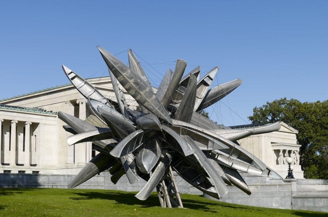 Set against a clear blue sky, this dynamic outdoor sculpture crafted from interconnected silver metal canoes commands attention in front of a classical-style stone building. Its a striking highlight among New York Sculpture Parks worth visiting, nestled on the lush green grass. Set against a clear blue sky, this dynamic outdoor sculpture crafted from interconnected silver metal canoes commands attention in front of a classical-style stone building. Its a striking highlight among New York Sculpture Parks worth visiting, nestled on the lush green grass.