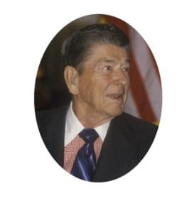 A man with short, dark hair wearing a dark suit, red and white checkered shirt, and a blue tie. He gazes to the side with a neutral expression, exuding a presidential air. An American flag is partially visible in the background. A man with short, dark hair wearing a dark suit, red and white checkered shirt, and a blue tie. He gazes to the side with a neutral expression, exuding a presidential air. An American flag is partially visible in the background.