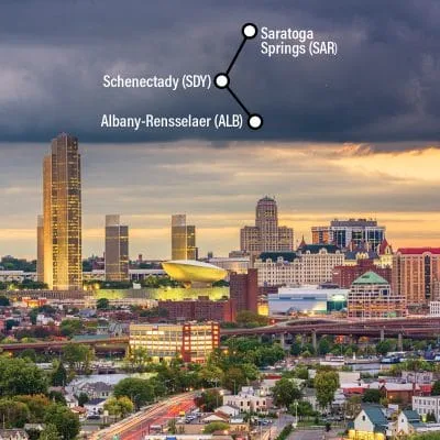 A cityscape of Albany, New York, captures tall buildings under a cloudy sky. A map overlay highlights train routes throughout the Capital Region, including Saratoga Springs and Schenectady, with corresponding station codes for easy navigation.