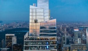 Aerial view of Summit One Vanderbilt, a tall, modern skyscraper with glass facades reflecting the dusky sky. The building reaches new heights with multiple terraces and is surrounded by a sprawling urban landscape, featuring a park visible in the background.