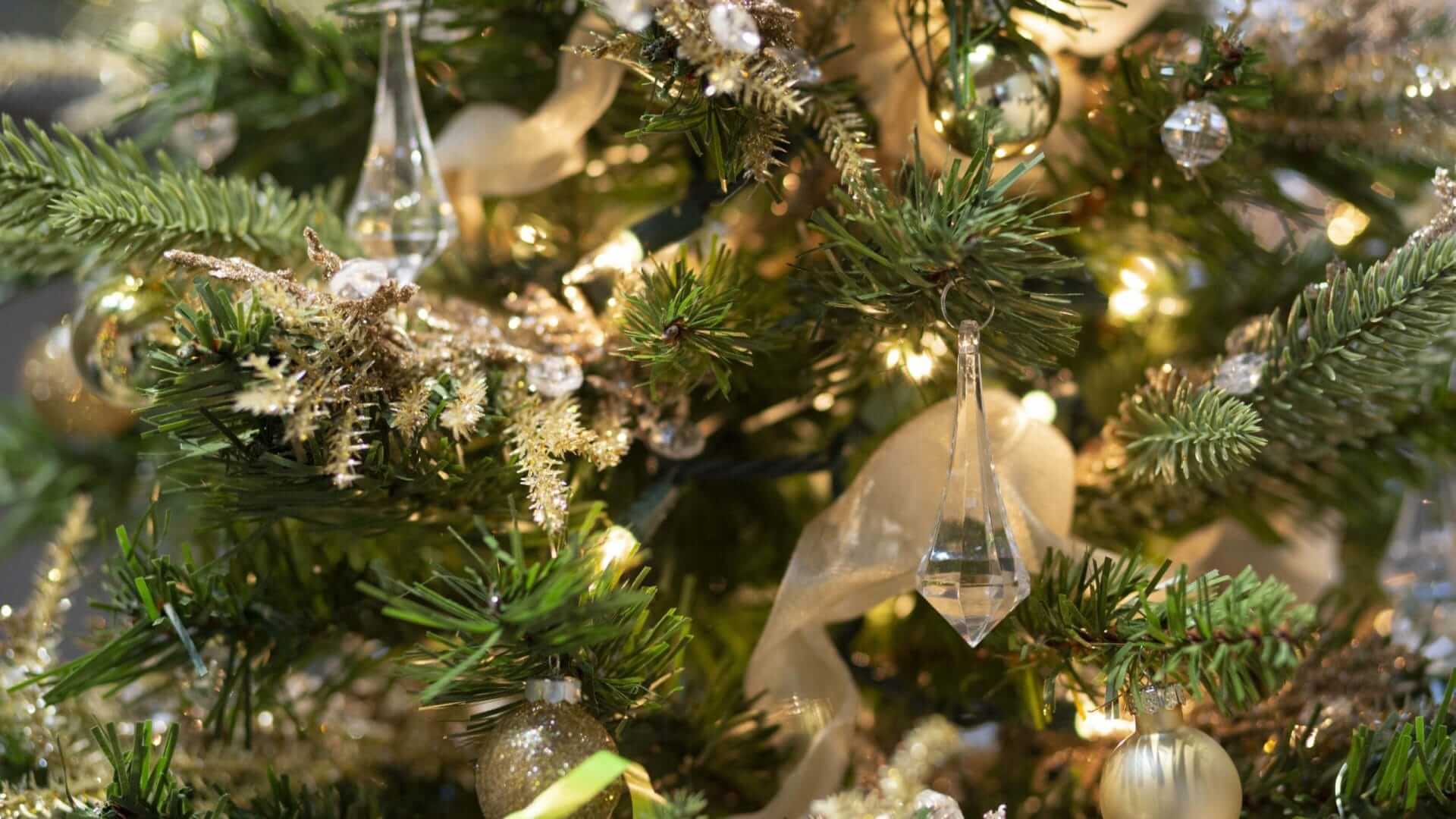 A close-up of a Christmas tree at the Festival of Trees and Light, adorned with gold and glass ornaments, shimmering lights, and ribbons. The decorations include baubles, delicate icicles, and shimmering garlands, creating a festive and elegant look.