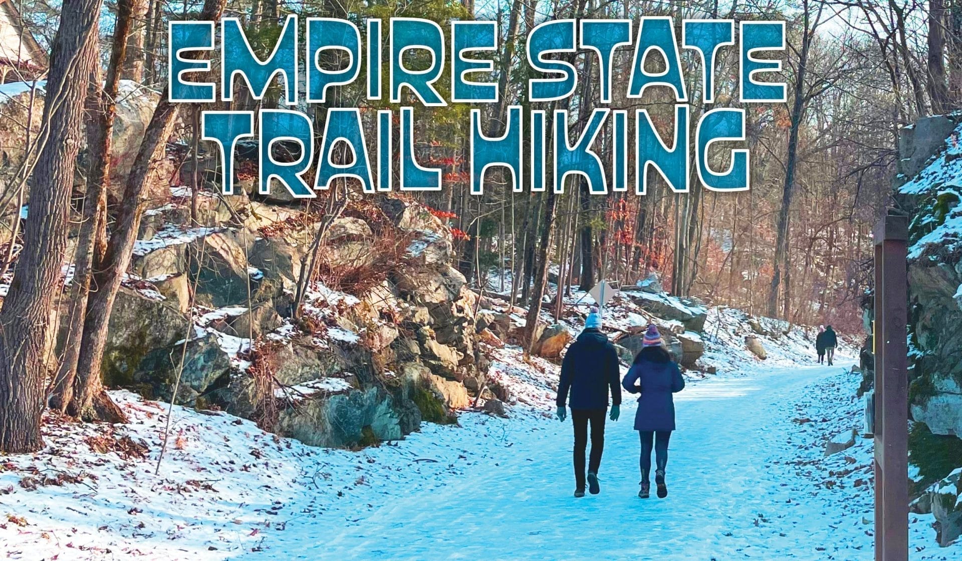 Two people walk down a snowy, wooded trail with rocky edges in winter on the Empire State Trail Hiking route. Large text, “Empire State Trail Hiking,” appears at the top while other hikers can be seen in the distance.