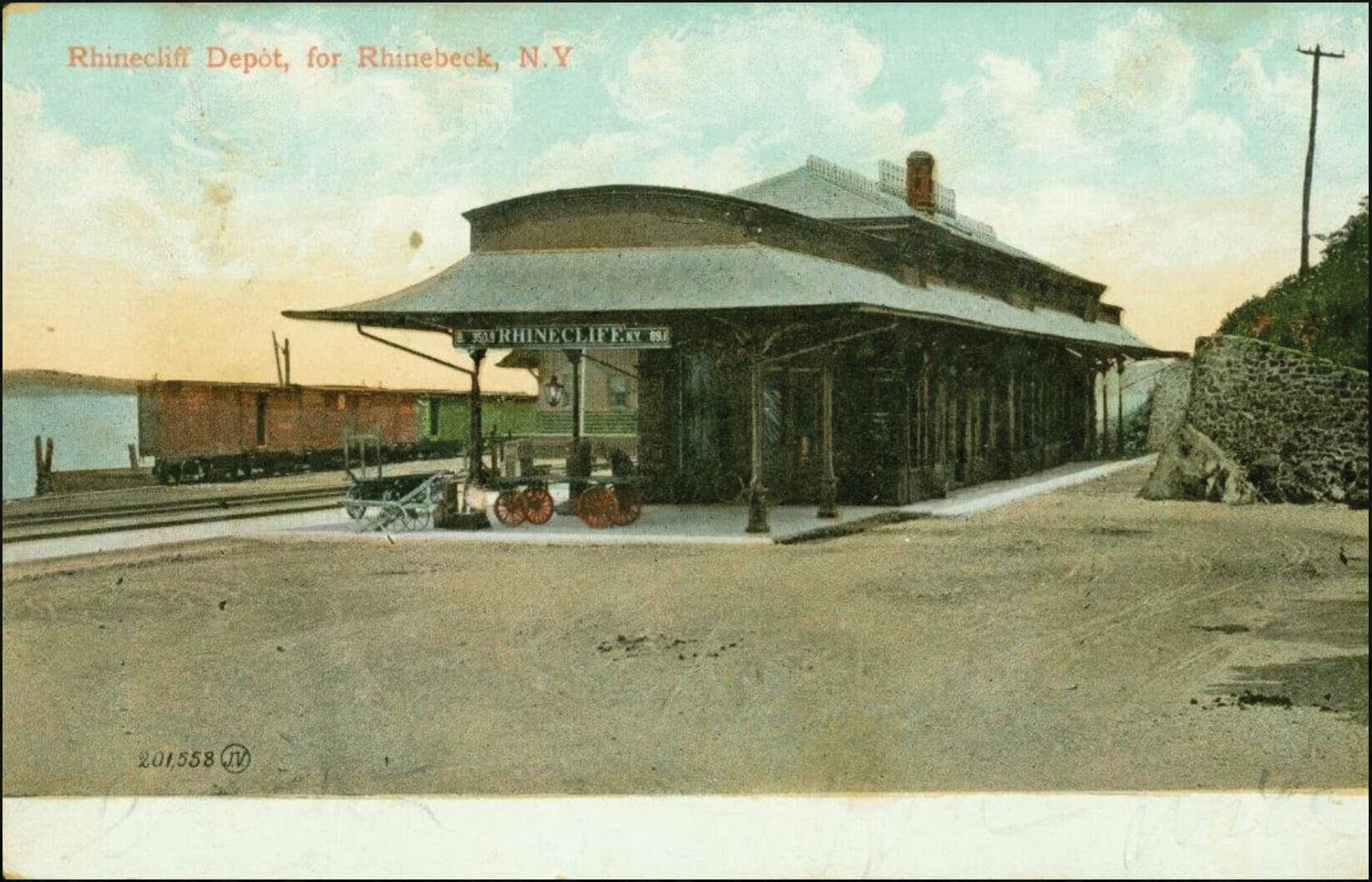Vintage postcard of the Rhinecliff Depot for Rhinebeck, NY, showing an old Amtrak train station with a covered platform, luggage carts, and tracks beside a body of water under a pastel sky.