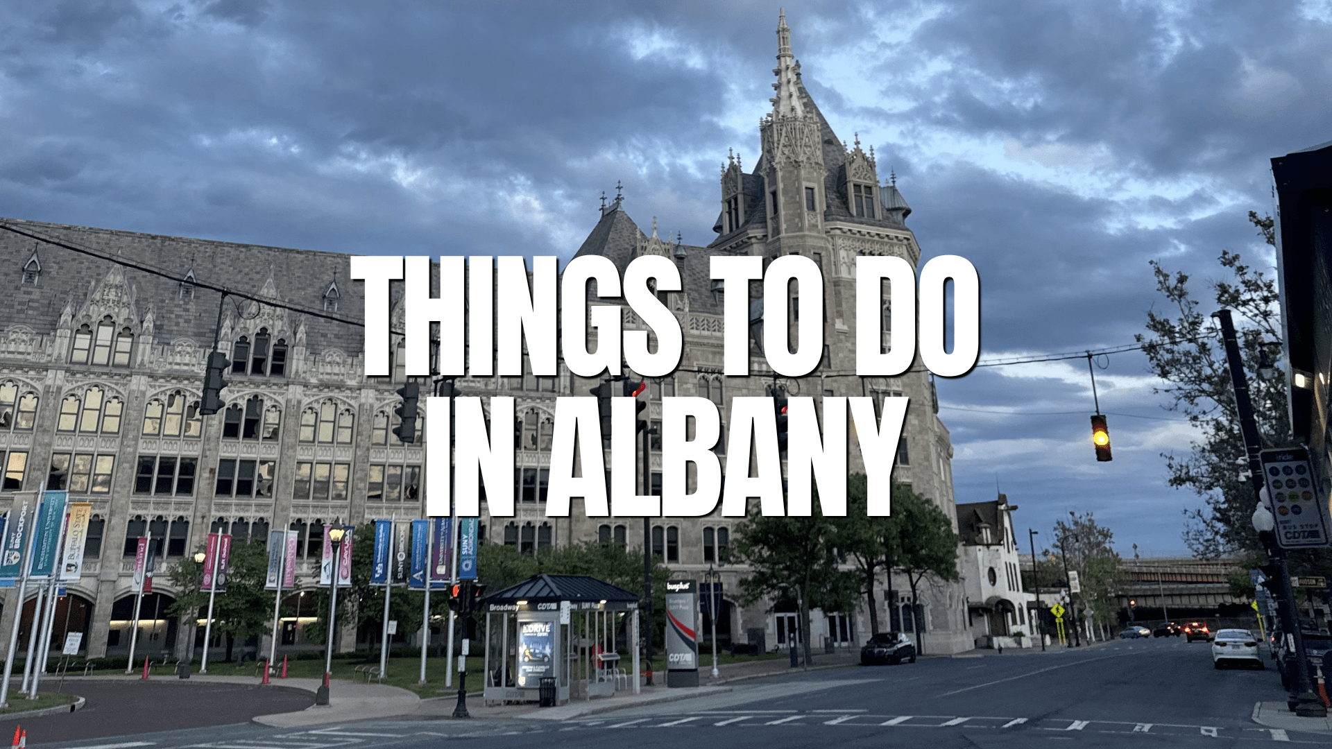A historic stone building in Albany under a cloudy evening sky, with streetlights and a bus stop near the Albany train station. Large white text across the image reads, THINGS TO DO IN ALBANY.