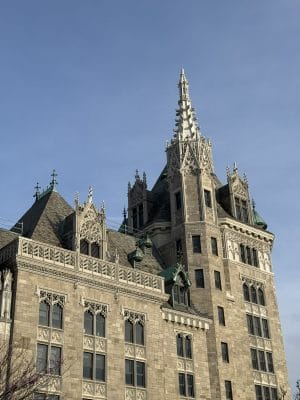 A historic stone building with ornate Gothic-style architecture, featuring pointed arches, decorative spires, and detailed carvings, set against a clear blue sky.
