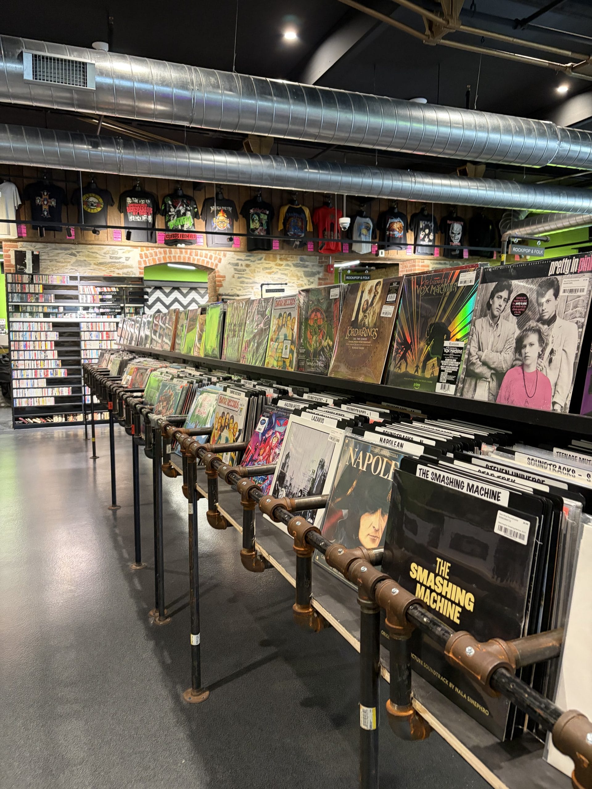 A record store interior with rows of vinyl records displayed in bins, album covers facing forward. Perfect for a Walking Tour of Poughkeepsie, the store features shelves of CDs, band merchandise, and an industrial decor style.