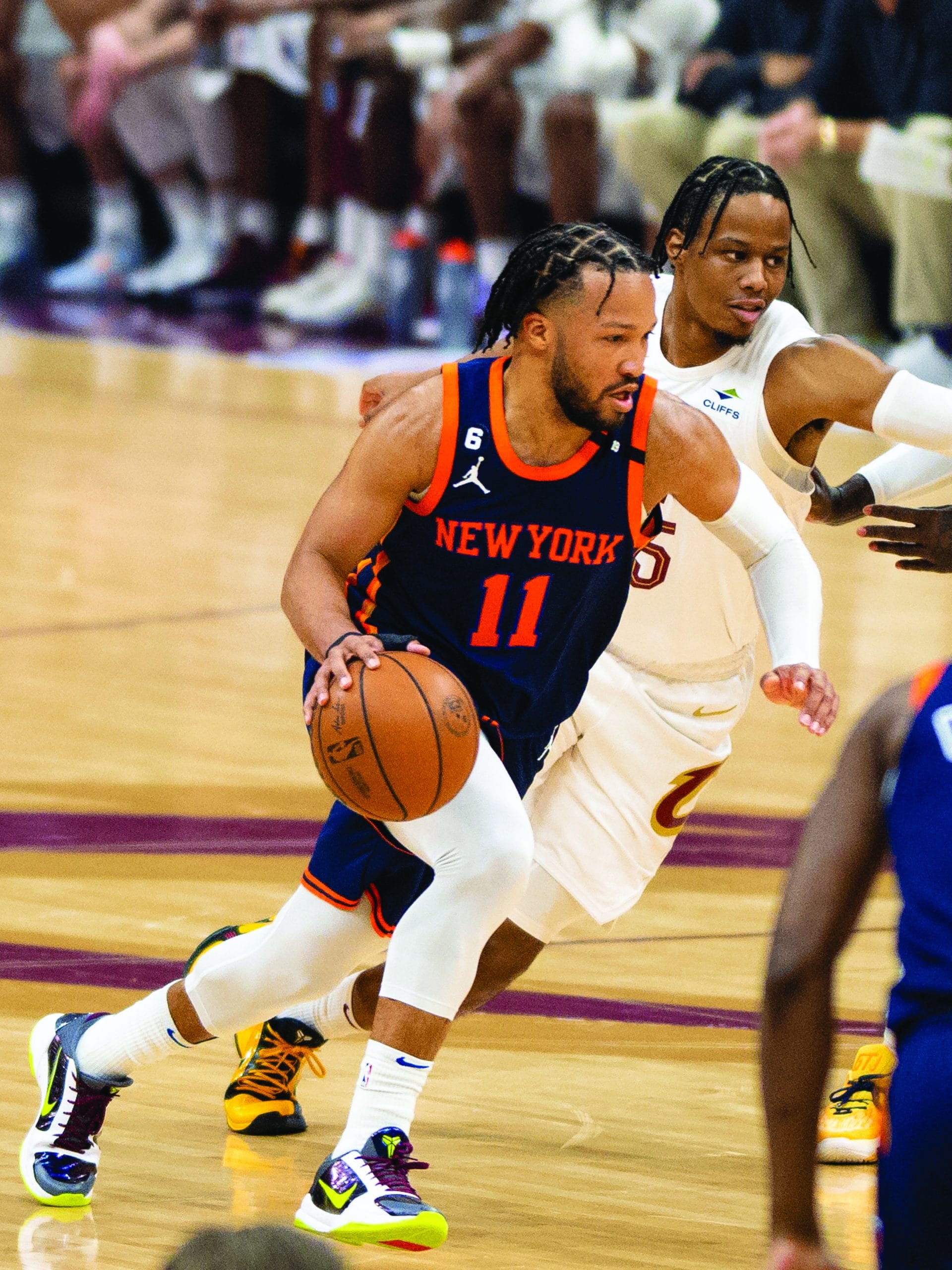 A New York Knicks player wearing jersey number 11 dribbles a basketball while being closely guarded by a Cleveland Cavaliers player during an NBA game, capturing the thrilling spirit of Wide World Of Sports on the basketball court.