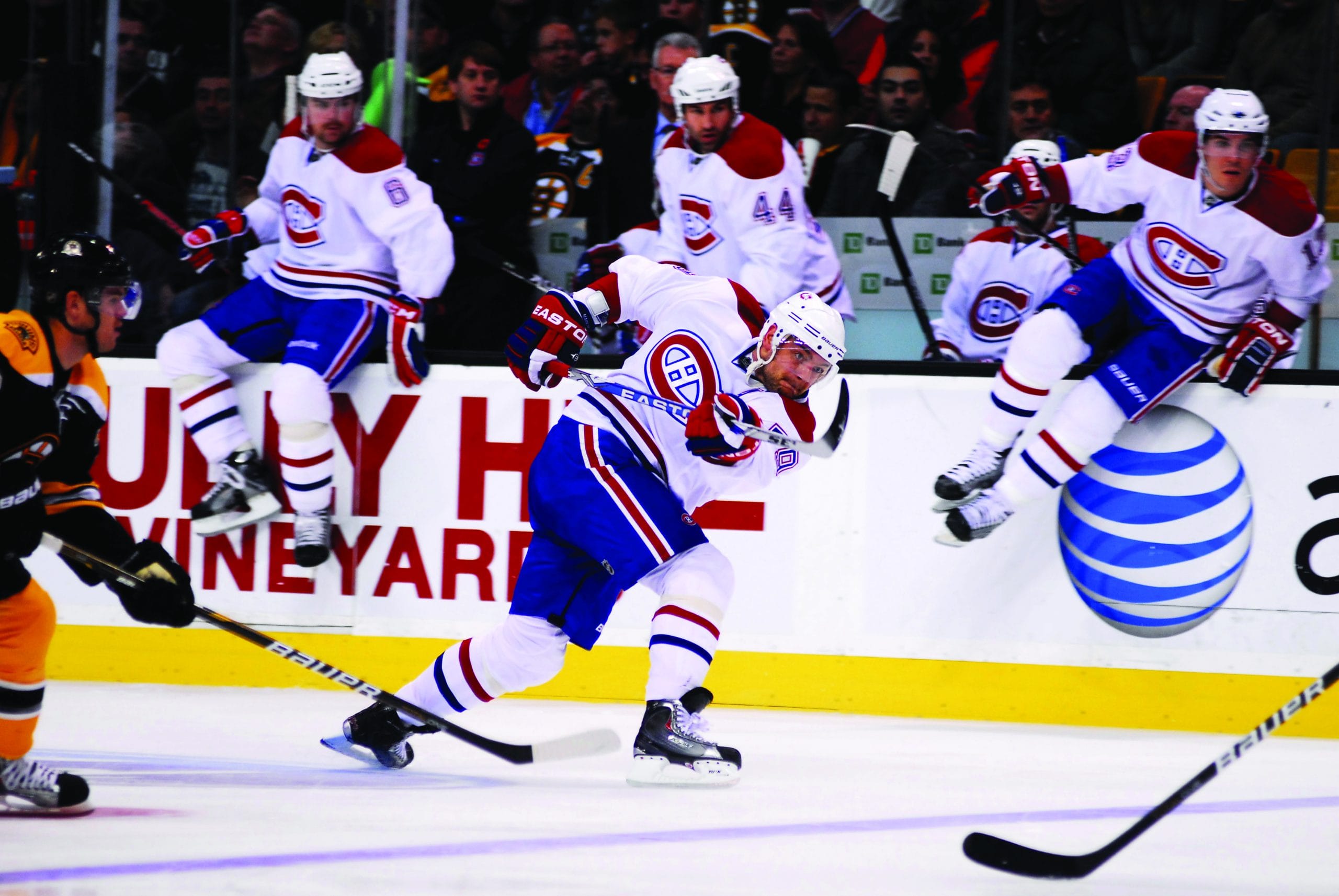 Montreal Canadiens hockey player skates quickly on the ice during a game, with teammates jumping over the boards and Wide World Of Sports fans watching from the stands in the background.