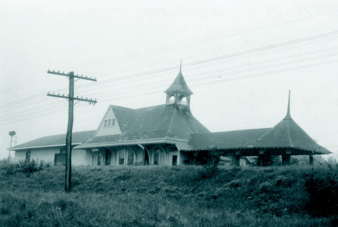 A black-and-white photo dated August 1962 shows the old Depot Theatre train station with a central tower, arched windows, and a wide overhanging roof. A telephone pole and grassy area are visible in the foreground.