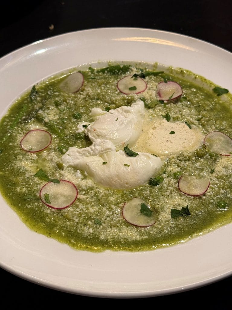 A white plate with green sauce, poached eggs in the center, and garnished with thinly sliced radishes, crumbled cheese, and fresh herbs—an elegant dish inspired by the charm of Miss New York Lake George.