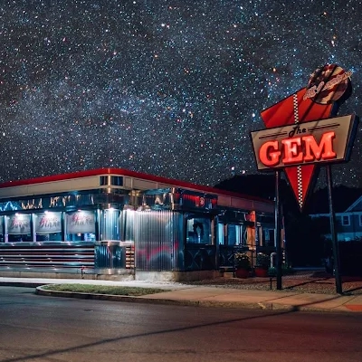 A retro diner in Syracuse with a neon “The GEM” sign glows overnight under a clear, star-filled sky, its metallic exterior reflecting the city lights—perfect for exploring after dark.