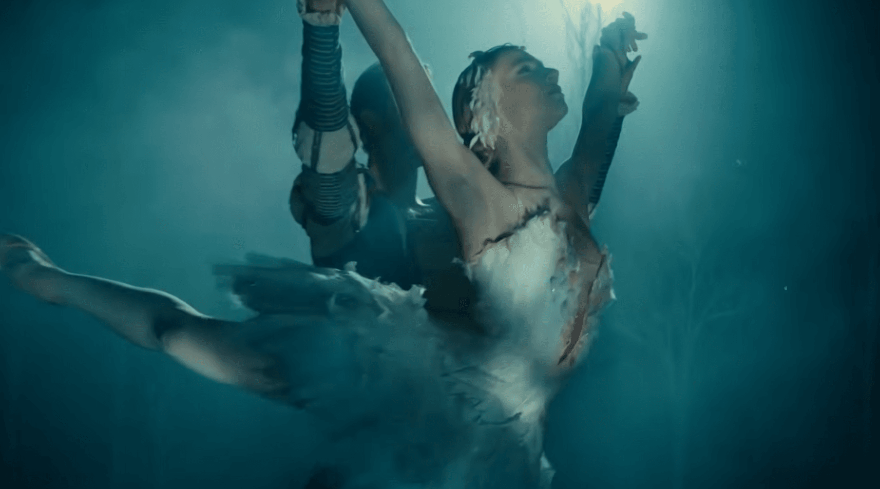 A ballerina in a white feathered costume performs an elegant lift with her masked partner during the American Ballet Theatre Summer Season, both illuminated by blue stage lighting and surrounded by mist for a dramatic, ethereal scene.