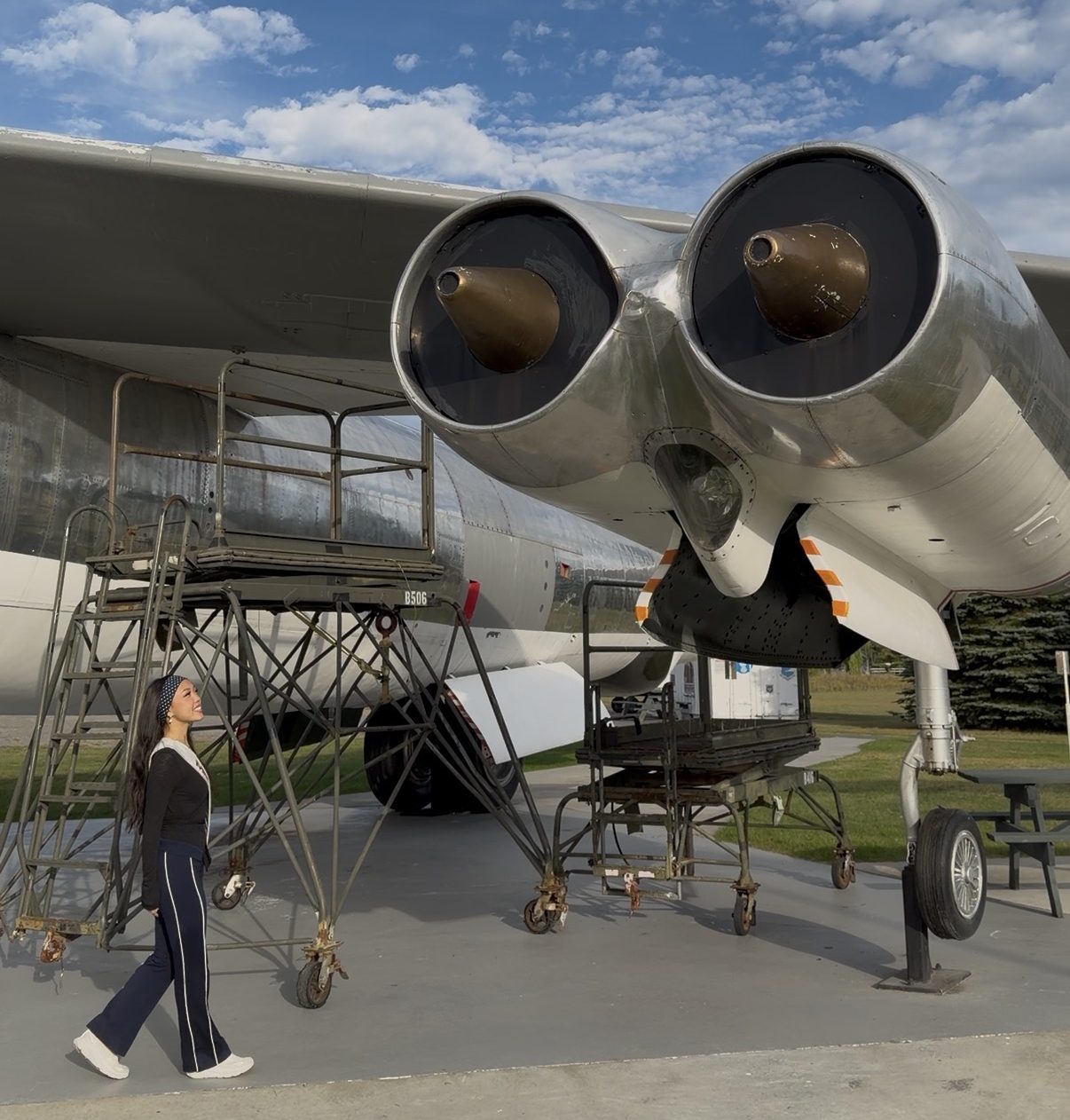 A person walks near a large jet plane with two rear-facing engines, standing on an outdoor display area under a partly cloudy sky as Miss New York explores Albany NY by Amtrak.