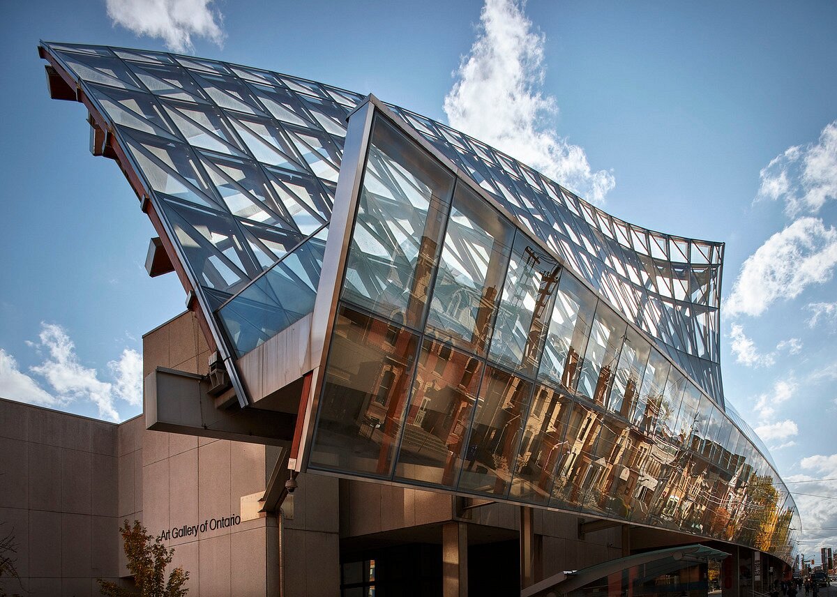 A modern glass and steel building facade with angular, sweeping lines reflects the city skyline under a blue sky with clouds, echoing the contemporary architecture found near Jardin Botanique De Montréal.