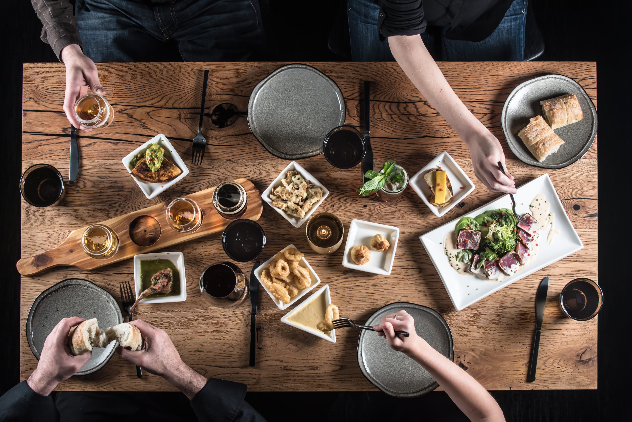 Overhead view of a wooden table with three people eating assorted appetizers, salad, bread, and drinks at Terrapin Restaurant. Plates, glasses, and small dishes are neatly arranged, showing a variety of foods in a social dining setting.